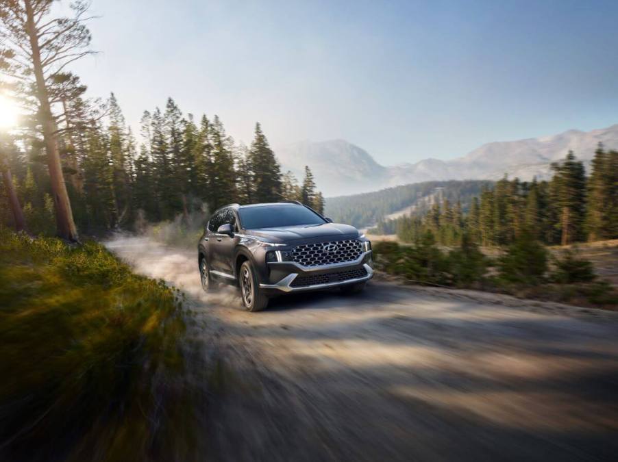 A 2023 Hyundai Santa Fe Hybrid midsize SUV model driving on a gravel road near forest trails