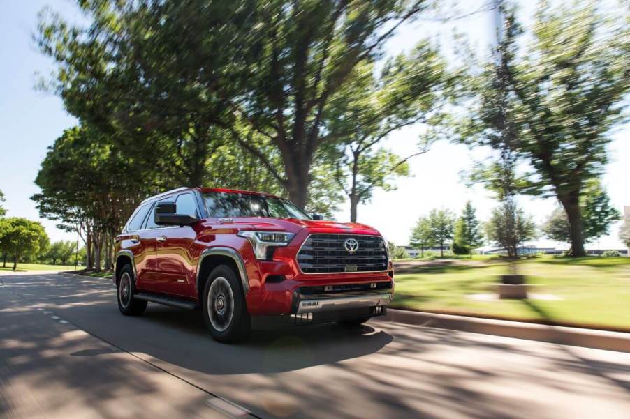 A 2023 Toyota Sequoia Limited full-size SUV model in Supersonic Red driving through a park