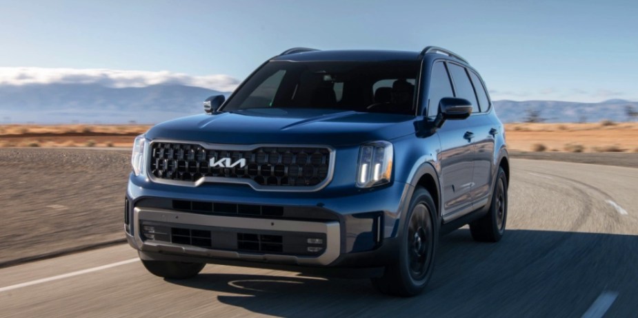 A blue 2023 Kia Telluride midsize SUV is driving on the road. 