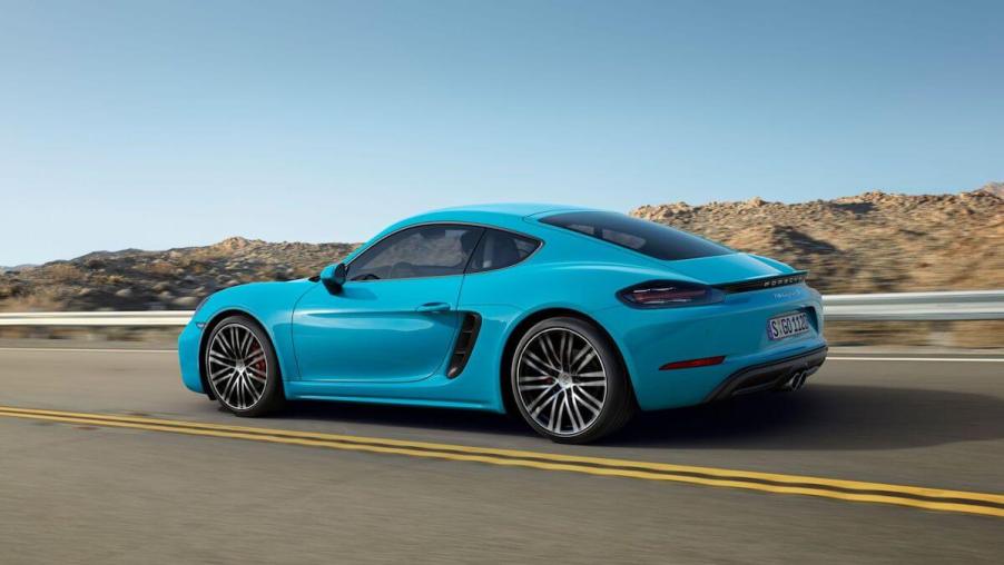 A blue Porsche 718 Cayman drives on a roadway.