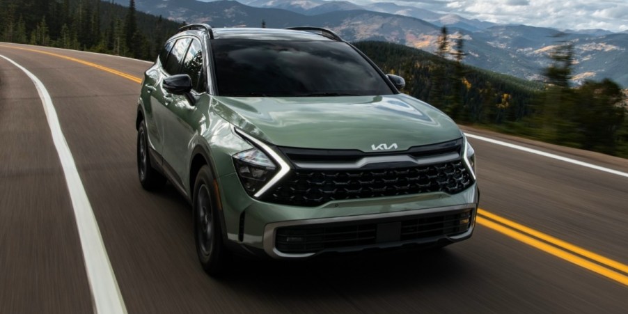 A green 2023 Kia Sportage small SUV is driving on the road.