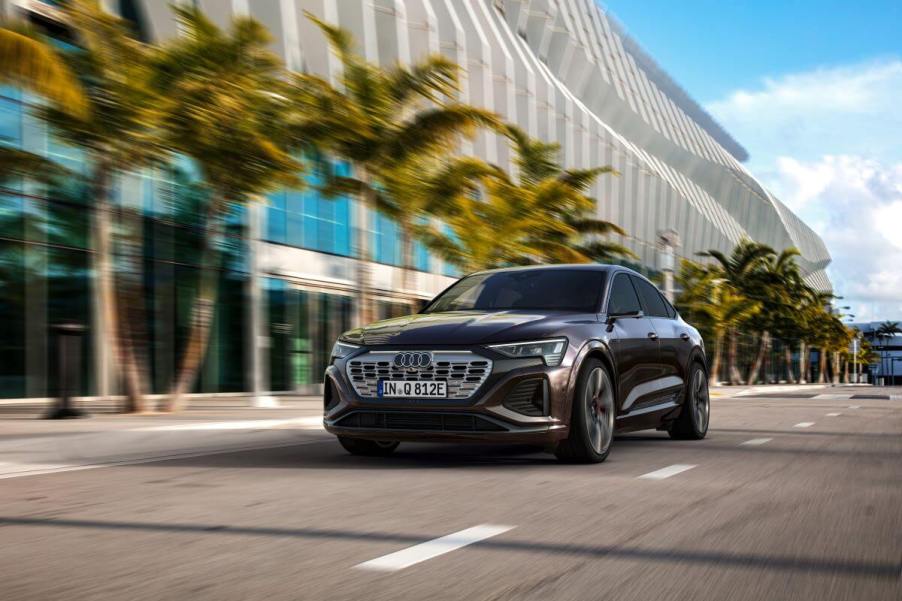 A 2024 Audi Q8 Sportback 55 e-tron quattro midsize SUV model driving past a line of palm trees outside a stadium