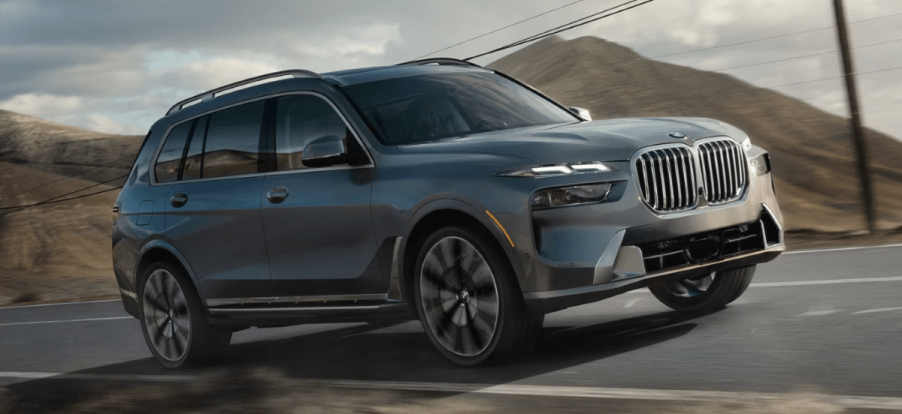 A 2024 BMW X7 full-size luxury SUV model driving down a country highway past phone lines