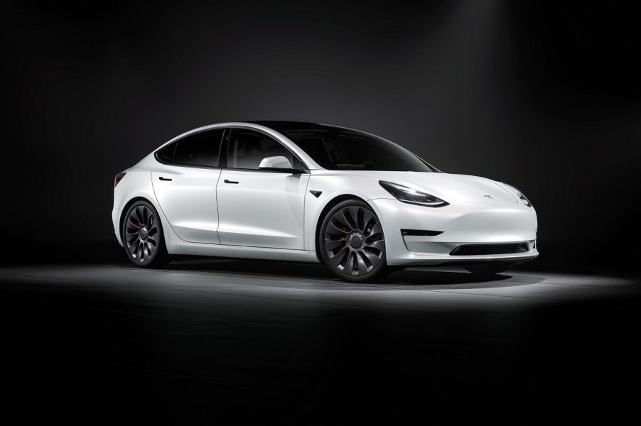 A white 2023 Tesla Model 3 parks under overhead lighting on a stage