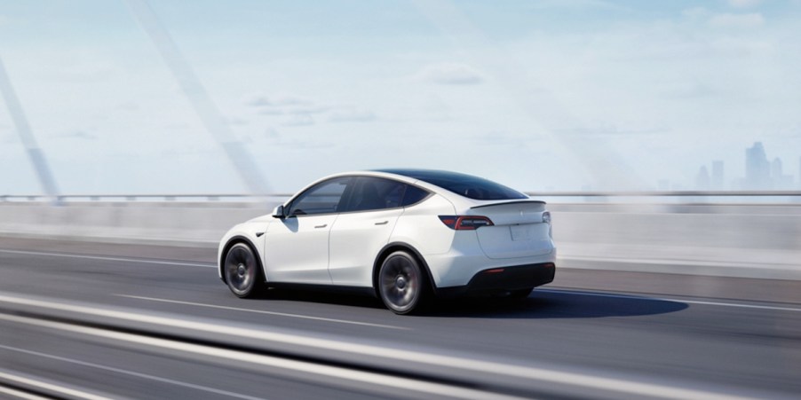 A white 2023 Tesla Model Y small electric SUV is driving on a bridge.