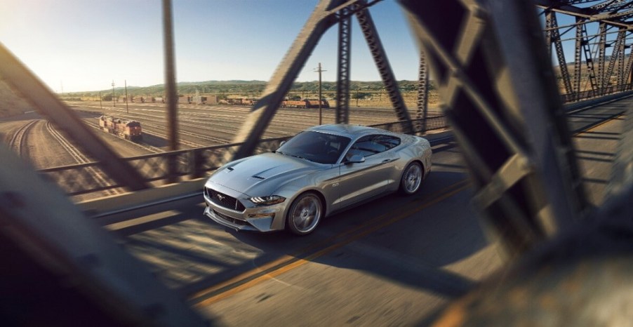 A silver S550 2023 Ford Mustang GT cruises on a city bridge.