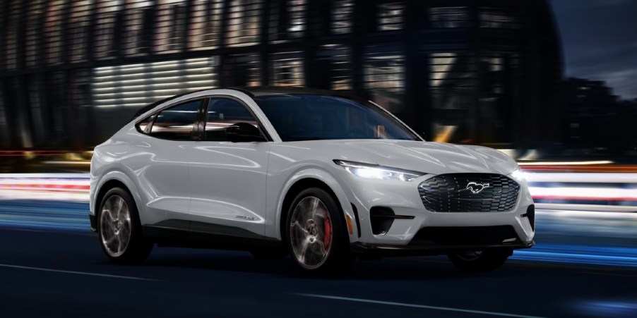 A white 2023 Ford Mustang Mach-E small electric SUV is driving on the road.