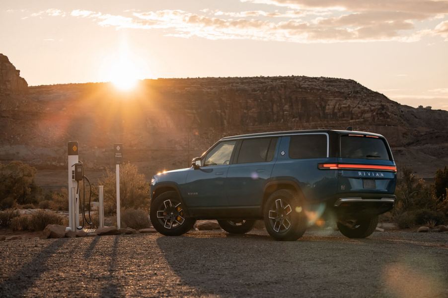 A blue Rivian R1S at a charging station in the desert at sunset. The Rivian R1S price isn't that bad compared to other luxury SUVs.