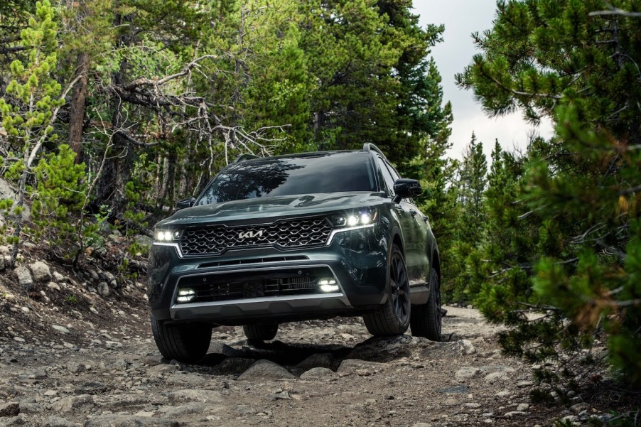 Green 2023 Kia Sorento driving through a trail in the woods. The Kia Sorento LX's price is pretty affordable.