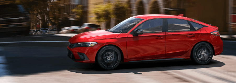 A side profile shot of a 2024 Honda Civic Hatchback model in Rallye Red driving through a city