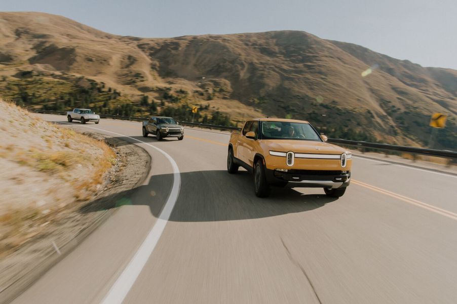 Three Rivian R1T models driving along a curved road by a cliff. The 2024 Rivian R1T is becoming a contender.