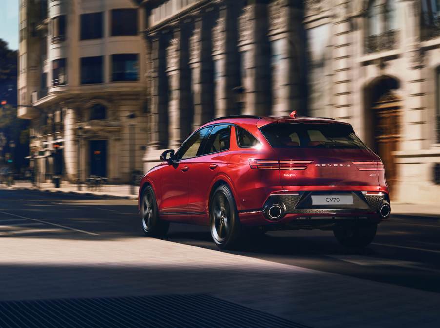 A red 2023 Genesis GV70 driving down a city road. The Genesis GV70's price is a big positive point.