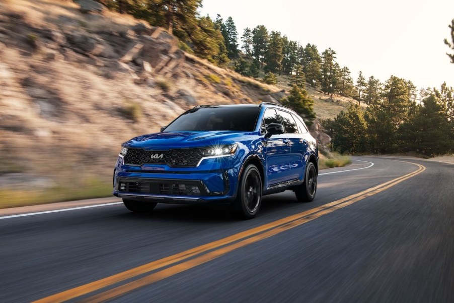 A blue 2023 Kia Sorento driving next to a hill. This Kia 3-row SUV is still a premium option.