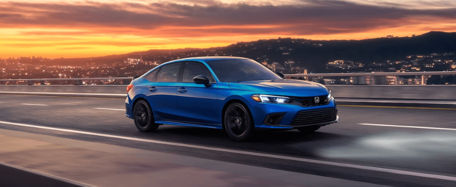 A 2024 Honda Civic Si sports sedan in Aegean Blue Metallic on a highway as the sun sets over a city