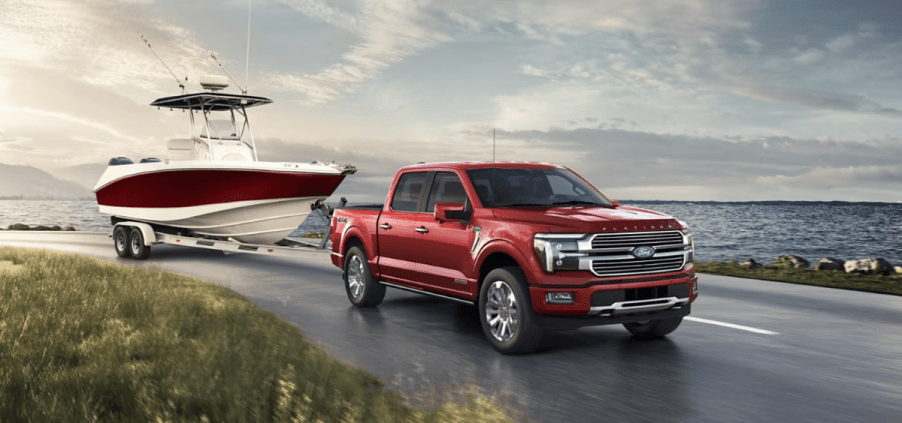 A 2024 Ford F-150 full-size pickup truck model towing a boat as it drive past a large lake of water