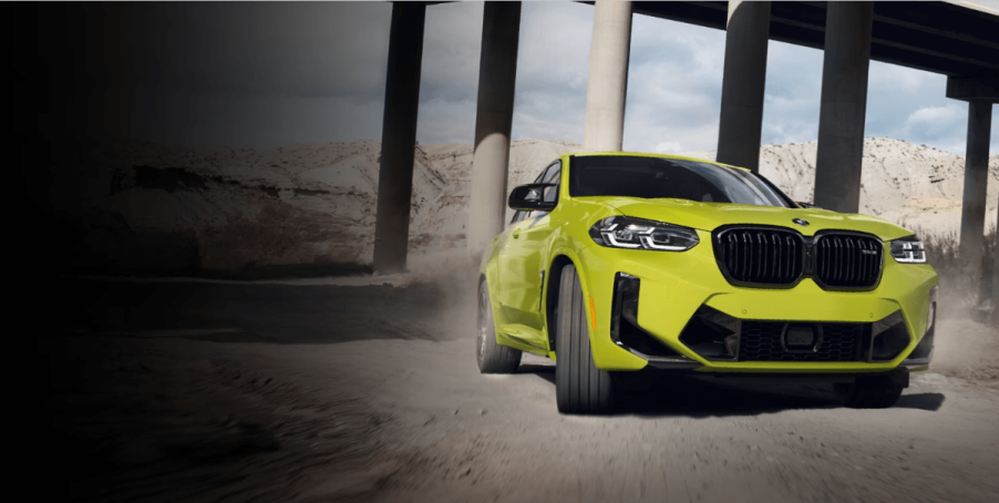 A BMW X4 M compact luxury performance-trimmed SUV model driving through concrete pillars under a bridge