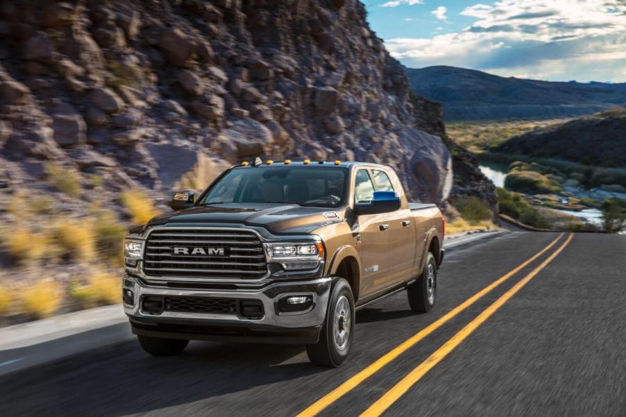 A 2024 Ram 2500 HD Limited Longhorn pickup truck driving on a country highway framed by rocky mountains