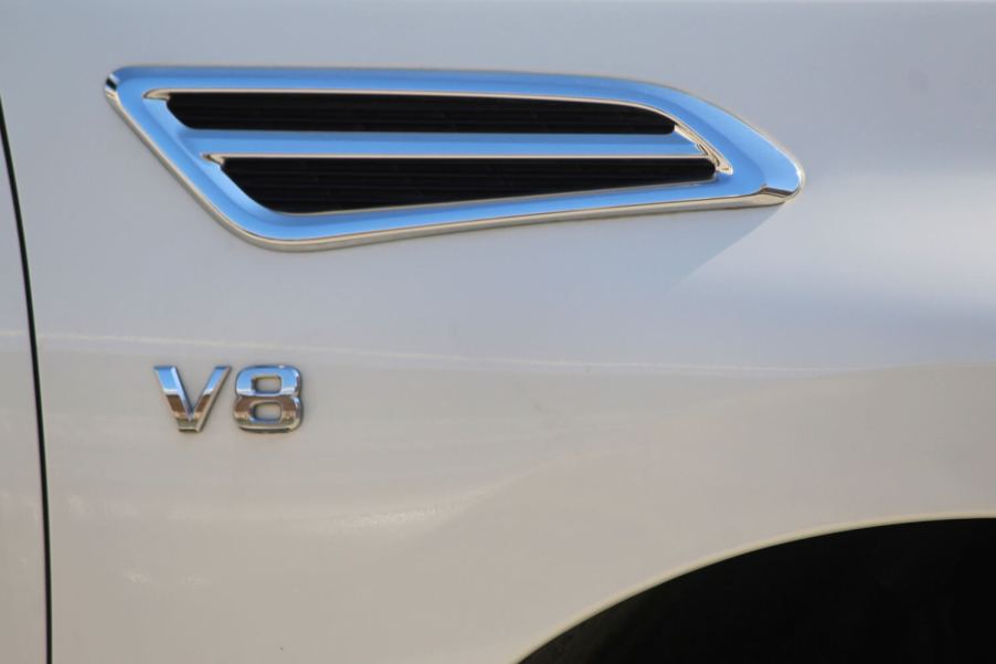 The chrome V8 badge on the fender of a white Nissan Titan pickup truck.