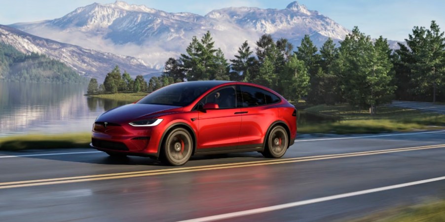 A red Tesla Model X midsize electric SUV is driving on the road.