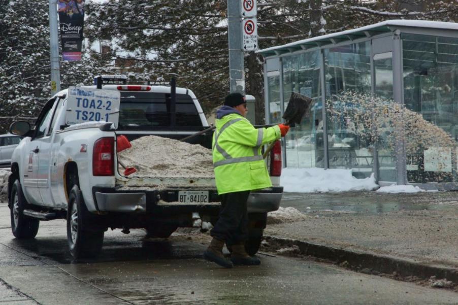 A worker pours road salt onto the street during winter.