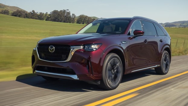 Plum-colored 2024 Mazda CX-90 three-row midsize SUV driving down a road.