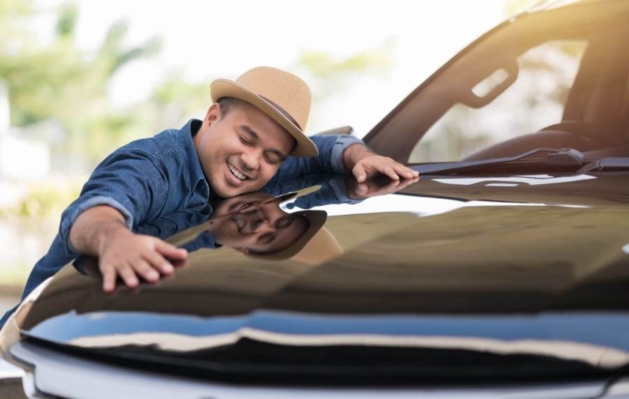 A car shopper smiles and hugs his car after finding it and gaining ownership.