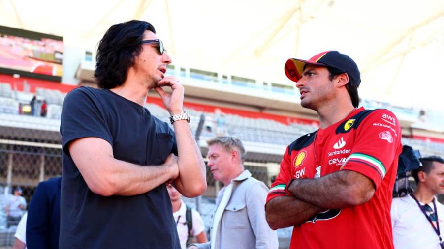 Adam Driver and Carlos Sainz chat in the pits at an F1 race.