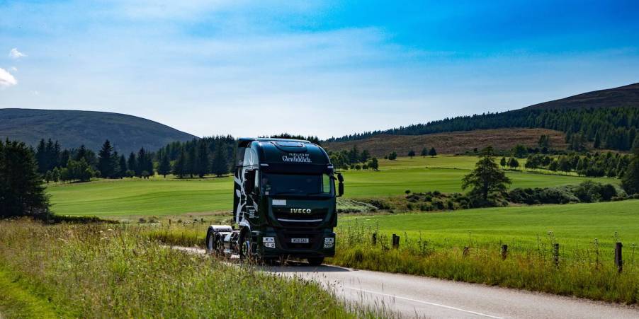 Green semi truck with no trailer driving through the Scottish countryside, powered by Whisky byproducts.