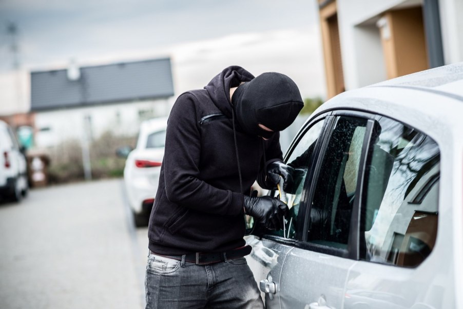 Man in a mask breaks into a silver car.