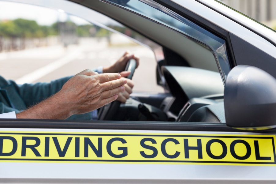 Pointing hand of a man riding along in student driver car.