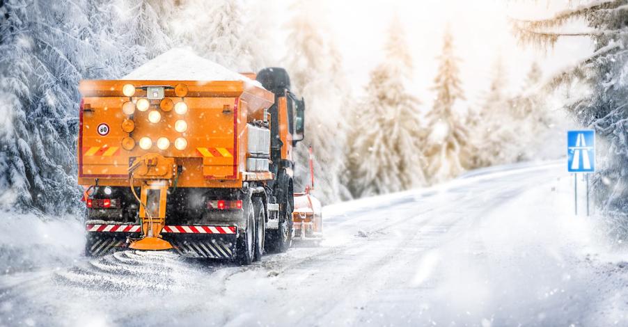 Dump truck spreads salt on a highway road during a winter snow storm