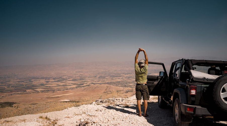 Man stands next to a parked Jeep during a roadtrip and stretches.