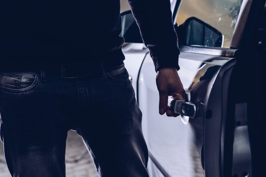 The hand of a thief opening the door of a silver Chevy Camaro