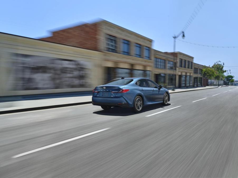 A blue 2025 Toyota Camry hybrid shows off its rear-end styling as it cruises a city street.