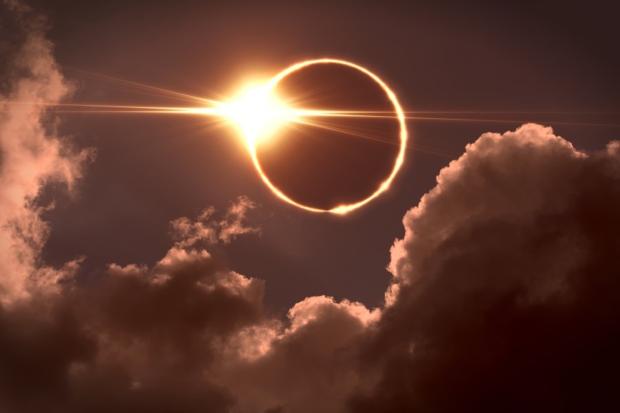 The sun disappearing behind the moon in a total solar eclipse, clouds visible in the foreground