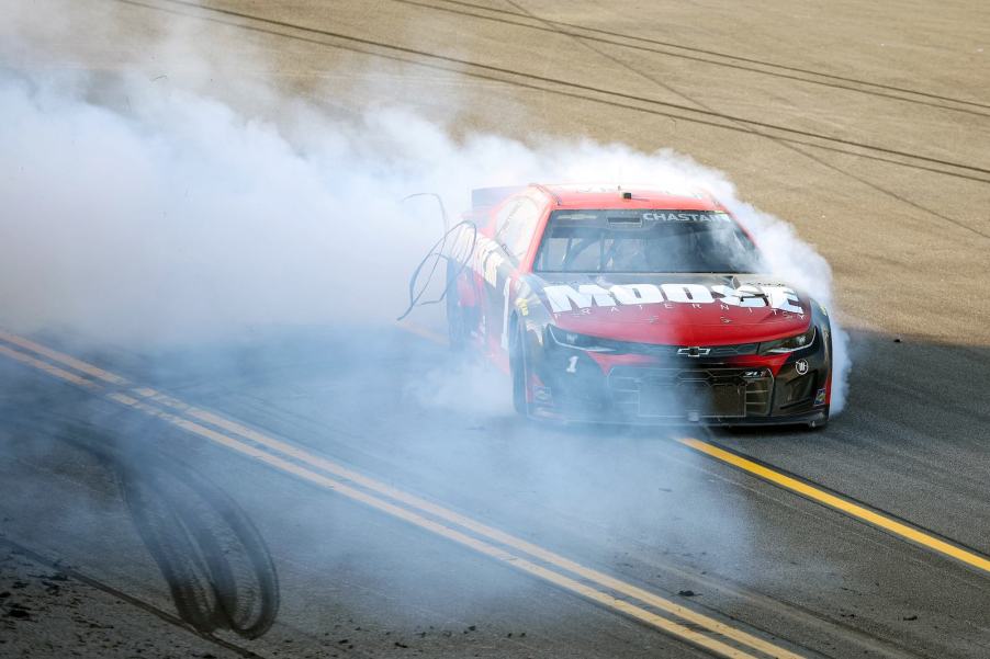 Red NASCAR car doing burnouts on the track