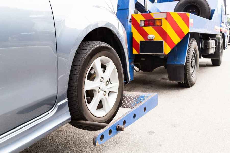 A blue tow truck carries a silver car shown in right rear side closeup angle view