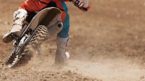 A closeup shot shows a person taking a ride on a dirt bike on a trail instead of the road.