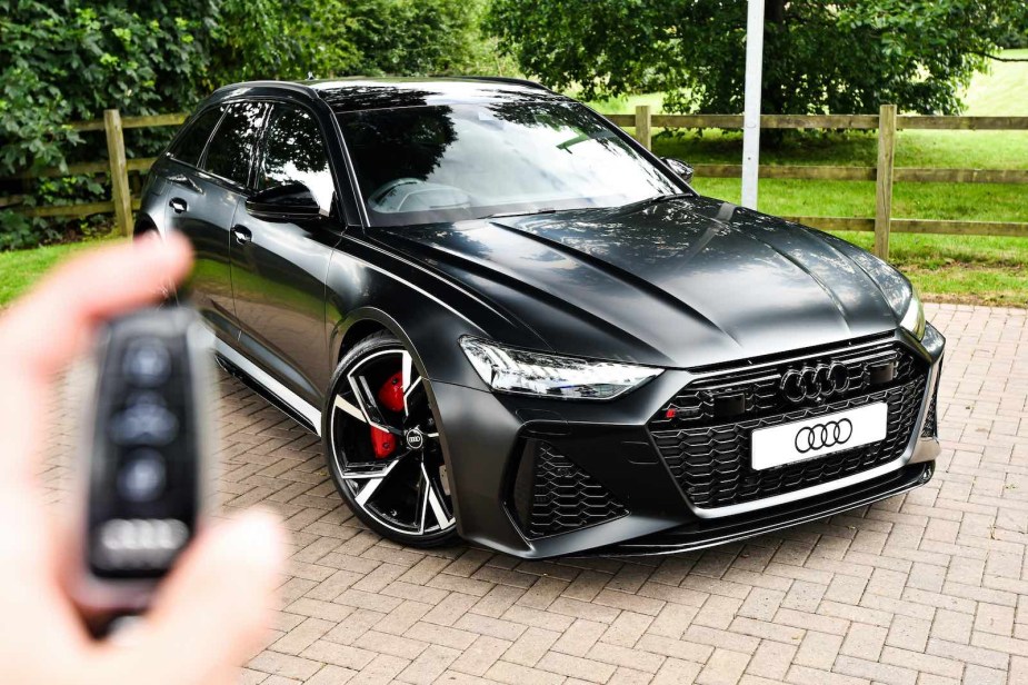 A wireless key fob held up in front of a black Audi wagon