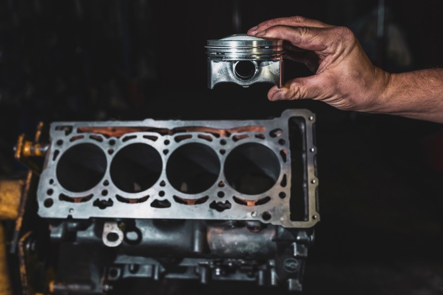 Hand holding a piston near a polished V8 engine block.