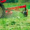 Grass clippings flying out of the deck of an orange lawn mower.