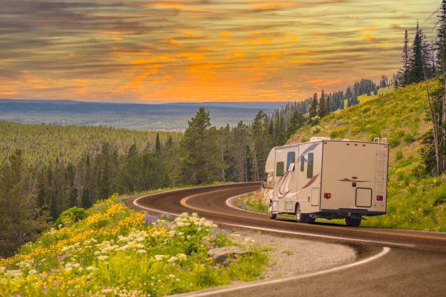 RV camper truck driving along a mountain road, the sun setting in the distance.