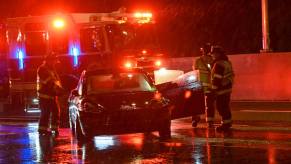 First responders gather around a crashed Tesla sedan parked on the interstate on a rainy night.