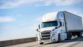 A white semi-truck driving down a highway with blue cloudy sky above