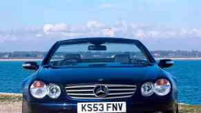 Mercedes-Benz supercar convertible parked in front of a blue ocean with its top down.