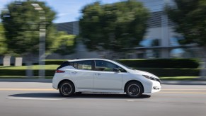 A white Nissan LEAF drives down an empty street.