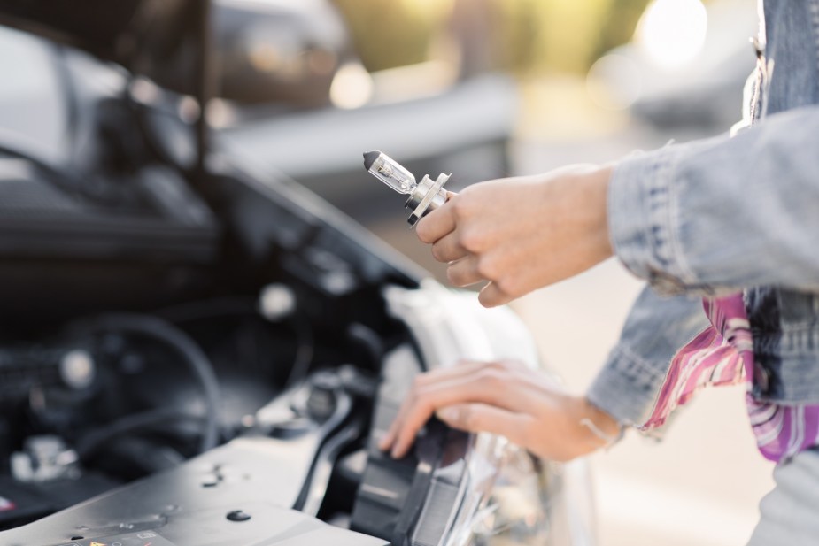 Woman changes the headlight bulb in her car.