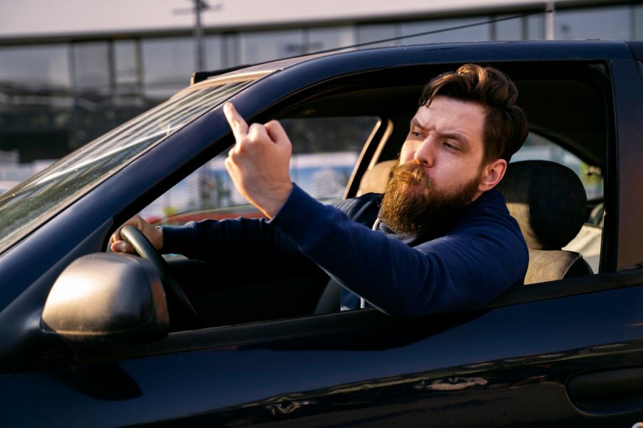 Bearded man giving the middle finger out an open car window.