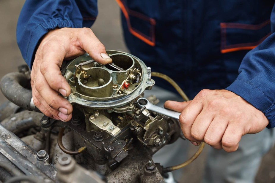 Mechanic twists a wrench to attach an engine's carburetor to its intake manifold.