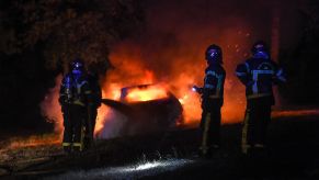 Three firefighters use a hose to extinguish a burning car